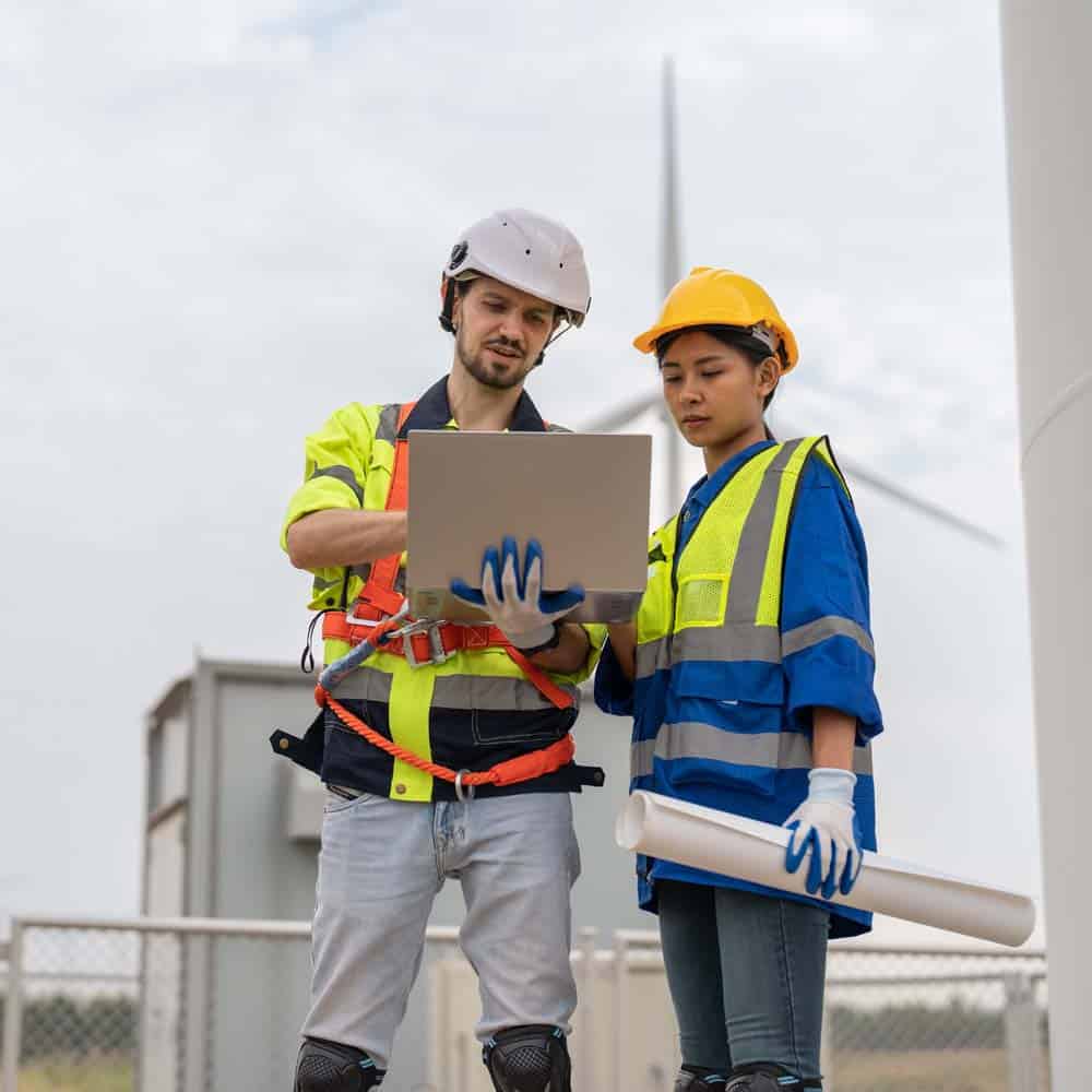 VPS. High Performance SSD VPS Hosting. Photo of a couple of workers using a laptop in the field with wind farm around them.